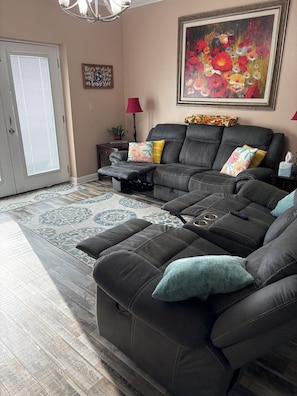 A living room with a sectional sofa, a painting, a lamp, and a door with blinds.