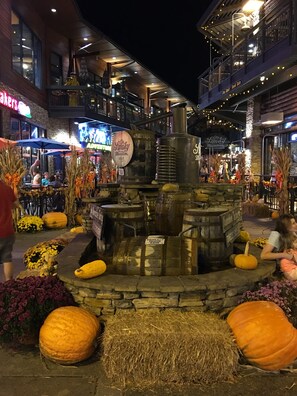 Une scène nocturne d’une place publique, avec un foyer central entouré de citrouilles et de bottes de foin.