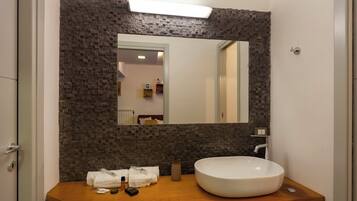 Un baño con pared de piedra, un espejo grande, tocador de madera y lavamanos blanco.