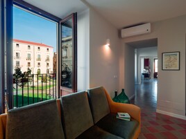 Una sala de estar moderna con un sofá, una puerta de cristal que da al exterior y un pasillo con un equipo de aire acondicionado.