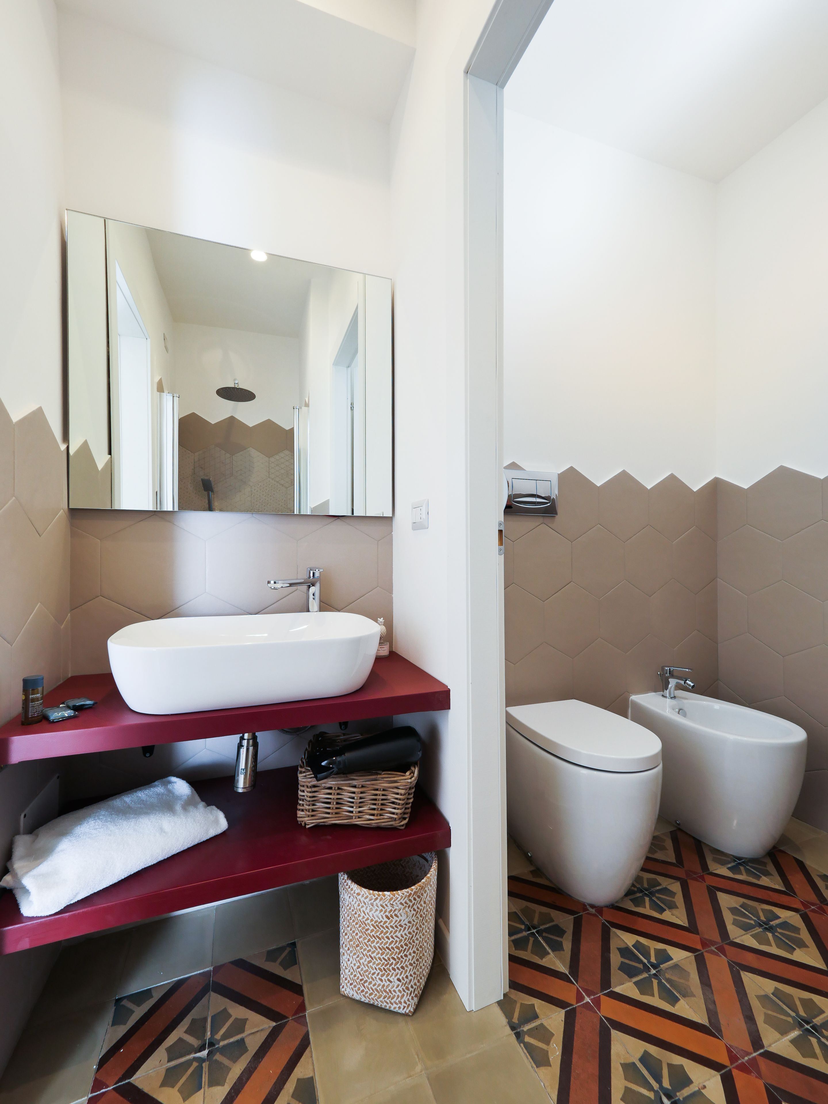 Casa de banho moderna com lavatório branco, toucador vermelho, espelho grande, bidé e azulejos de chão estampados.