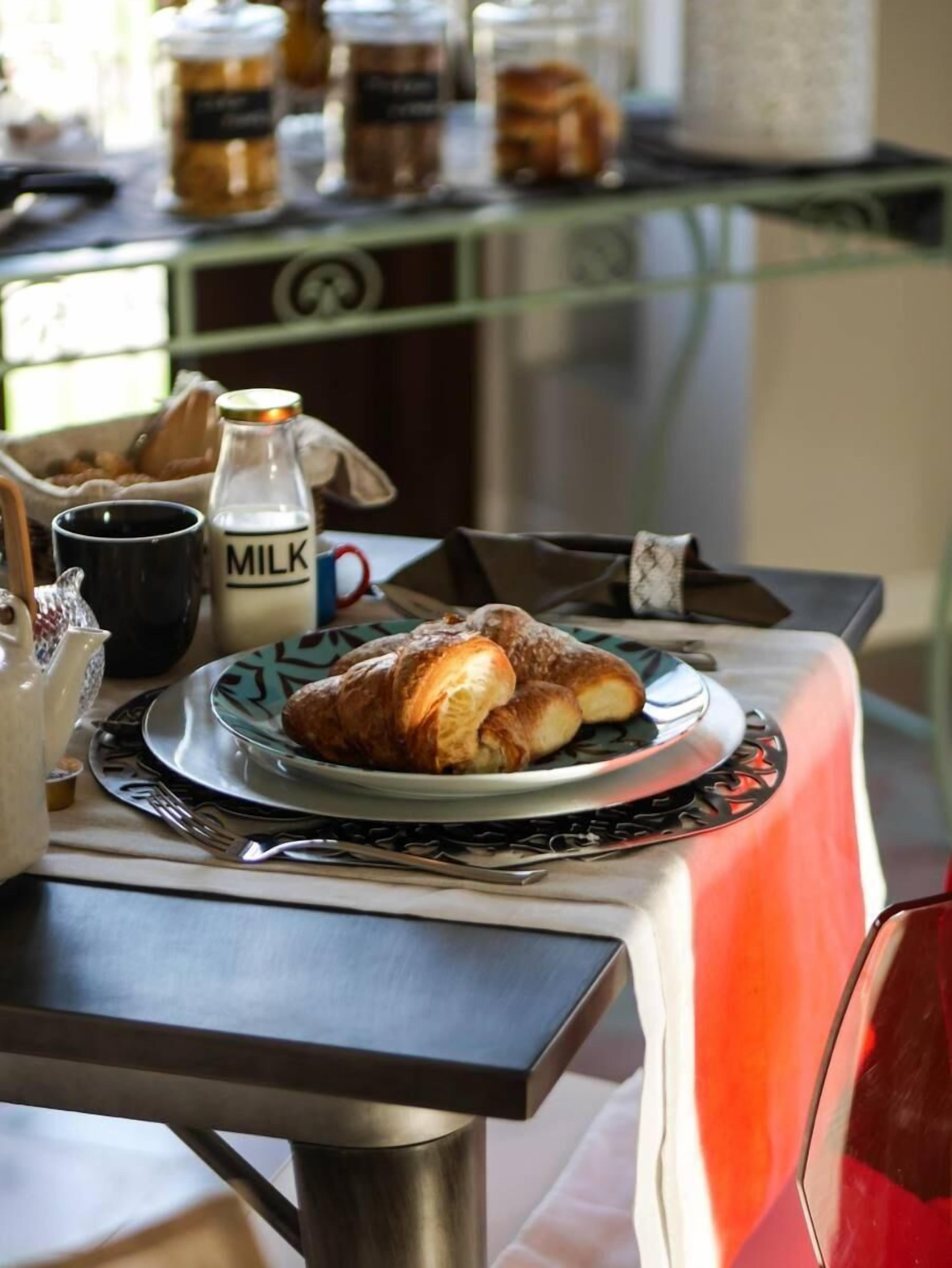 A breakfast setting with croissants on a plate, a milk bottle, and a coffee mug on a table.