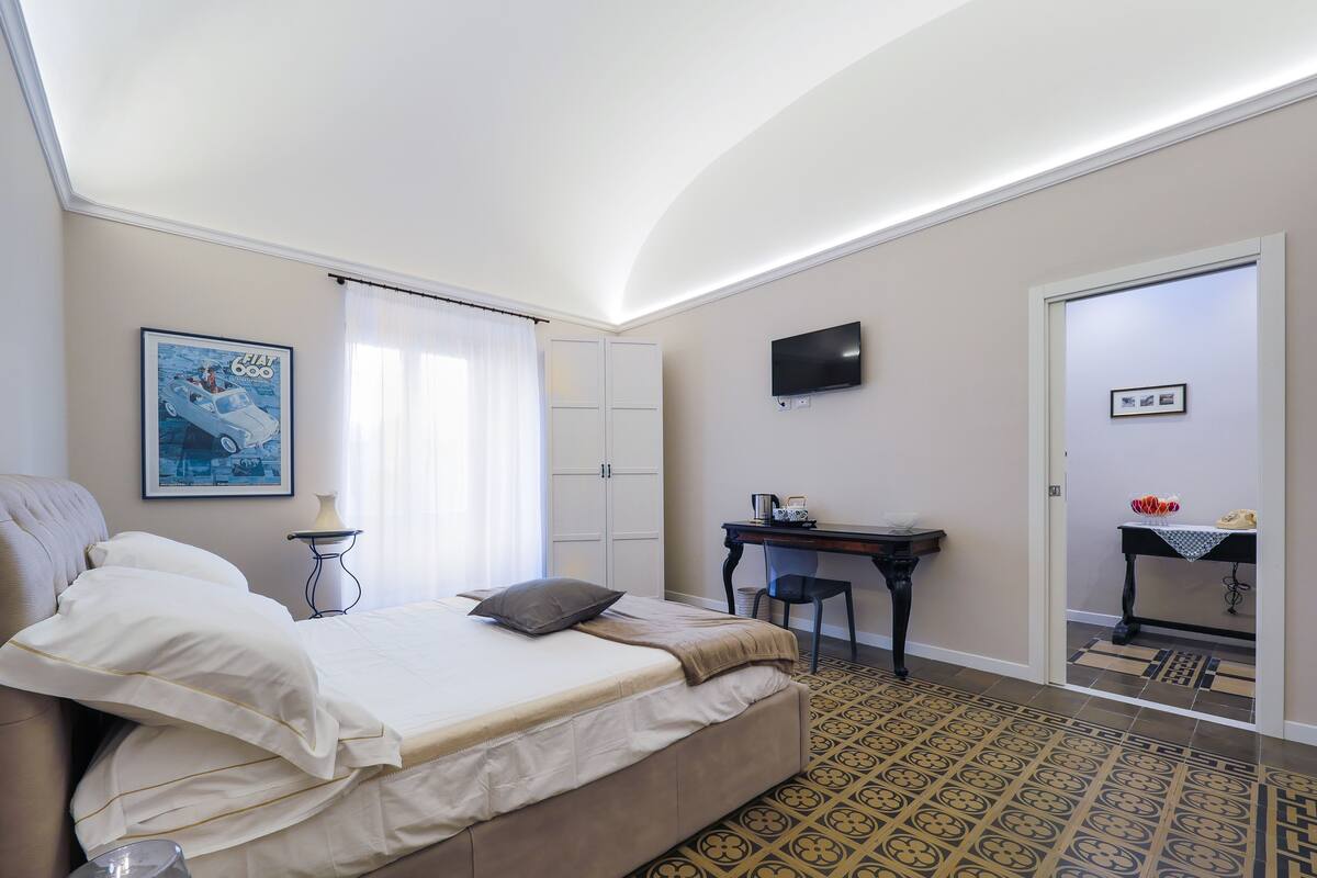 A bedroom with a bed, a desk, a chair, a television, and a patterned floor.
