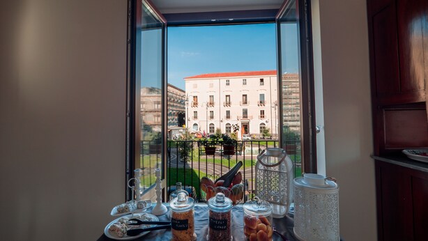 A table with food items and a view of a building through a window. - Sciara Larmisi (Catania)
