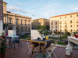 Una terraza con una mesa para dos, una planta en maceta y vistas a edificios históricos.