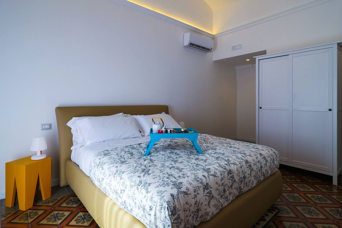 A neatly made bed with a floral bedspread, a bedside table with a lamp, and a wardrobe.