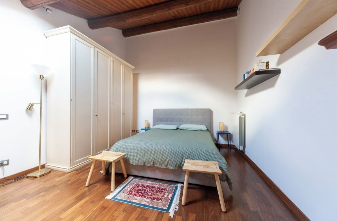A bedroom with a bed, bedside tables, a floor lamp, a radiator, and a wardrobe.