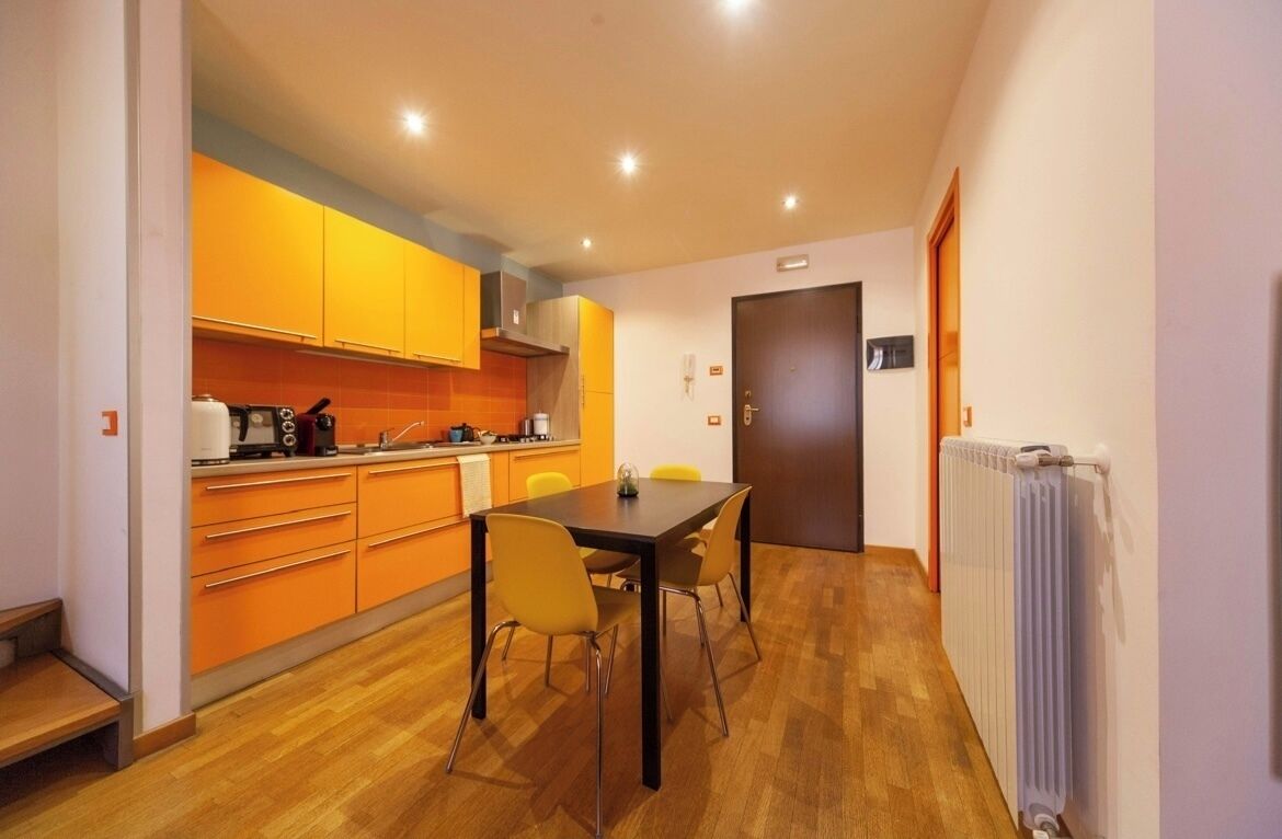 Una cocina moderna con armarios color naranja, una mesa de comedor con cuatro sillas y una puerta a la vista.