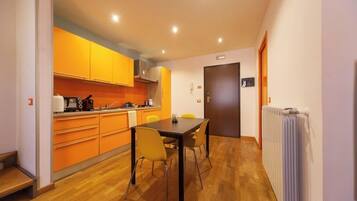 Una cocina moderna con armarios color naranja, una mesa de comedor con cuatro sillas y una puerta a la vista.
