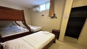 A bedroom with two wooden beds, a small bedside table, a wall-mounted air conditioner, a window with a curtain, and a door with a black handle. - Hostal Posada Del Sol (Guayaquil)