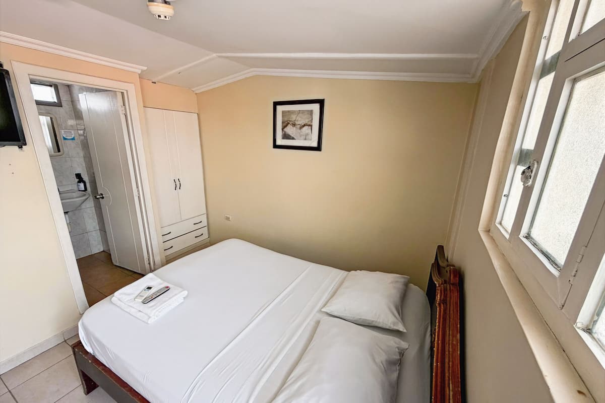 A bedroom with a bed, a wardrobe, a framed picture on the wall, and a window.