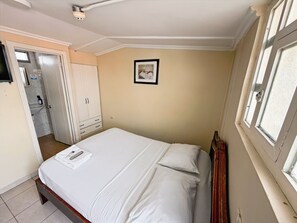 Een slaapkamer met een bed, een kledingkast, een lijst met een afbeelding aan de muur en een raam.