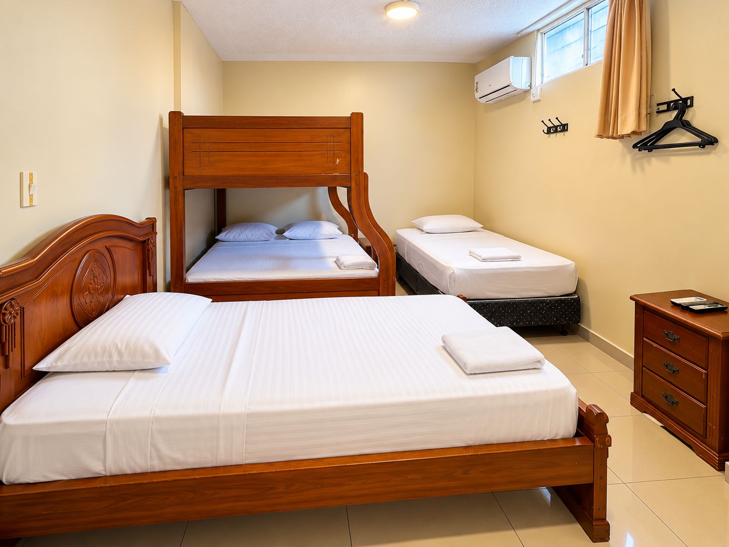 Una habitación de hotel con una cama grande, una cama más pequeña, un aparador de madera y un equipo de aire acondicionado.