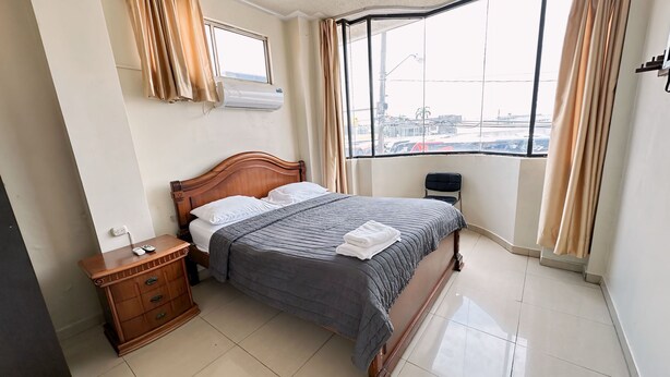 A neatly arranged hotel room with a bed, bedside table, and a window with curtains. - Hostal Posada Del Sol (Guayaquil)