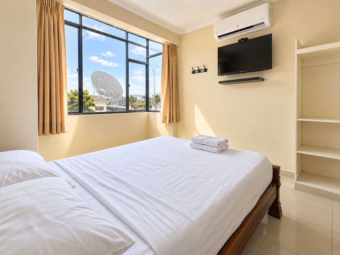 Una habitación de hotel con cama, televisor y ventana con cortinas.