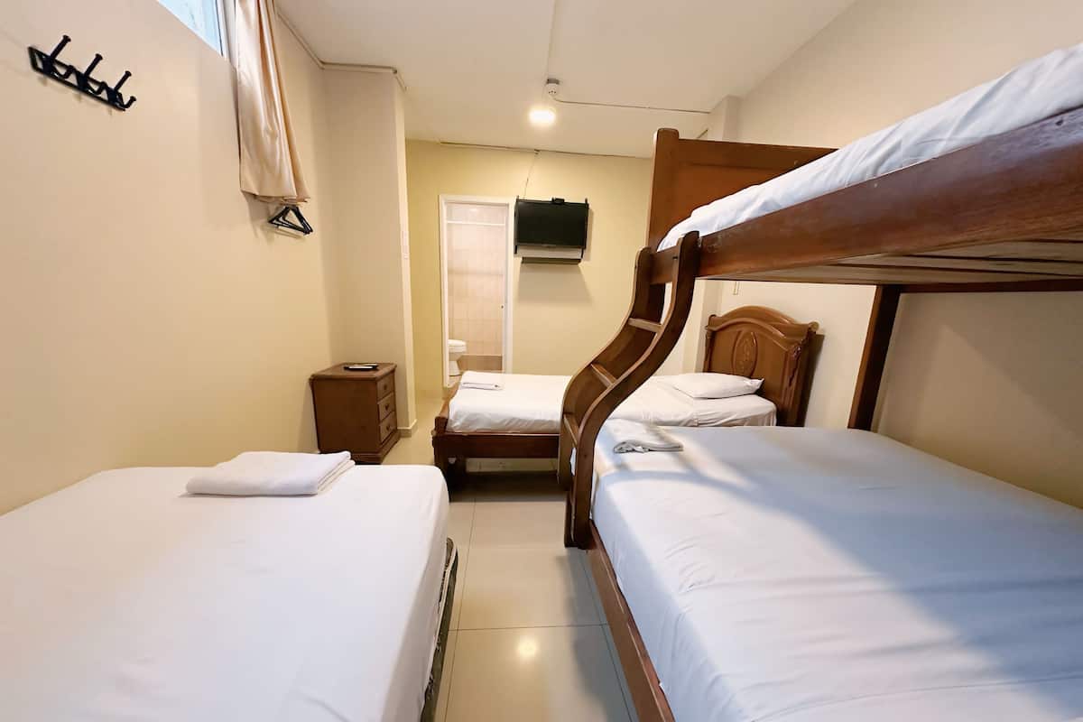 A hotel room with two single beds, a wooden headboard, a small wooden dresser, a wall-mounted TV, and a window with curtains.