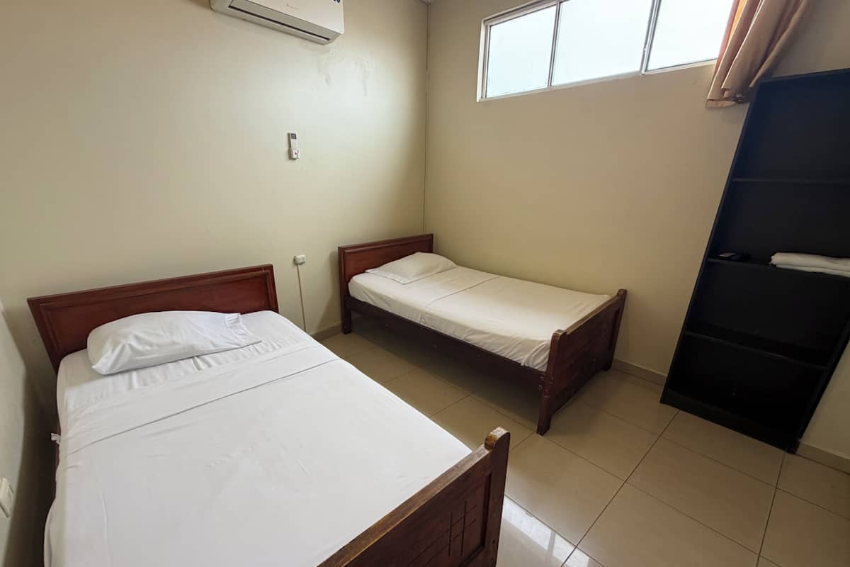 A bedroom with two wooden beds, a window, and a black wardrobe.