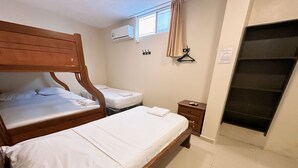 A hotel room with two wooden beds, a small bedside table, a wall-mounted air conditioner, a window with a curtain, and a door with a black handle. - Hostal Posada Del Sol (Guayaquil)