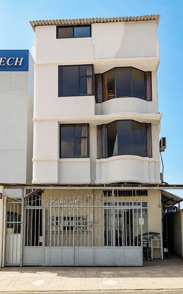 Un immeuble à plusieurs étages doté d’une entrée sécurisée par un portail, de grandes fenêtres et d’une enseigne indiquant qu’il s’agit d’un hôtel.