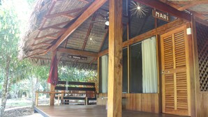 A wooden building with a thatched roof, a wooden door with a nameplate, and a bench outside. - La Habana Amazon Reserve (Tambopata)