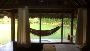 A room with a bed, a hammock, and a view of a grassy area with trees. - La Habana Amazon Reserve (Tambopata)
