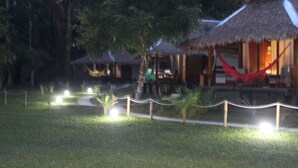 A thatched-roof structure with a hammock, surrounded by a well-lit garden with small plants and a pathway. - La Habana Amazon Reserve (Tambopata)
