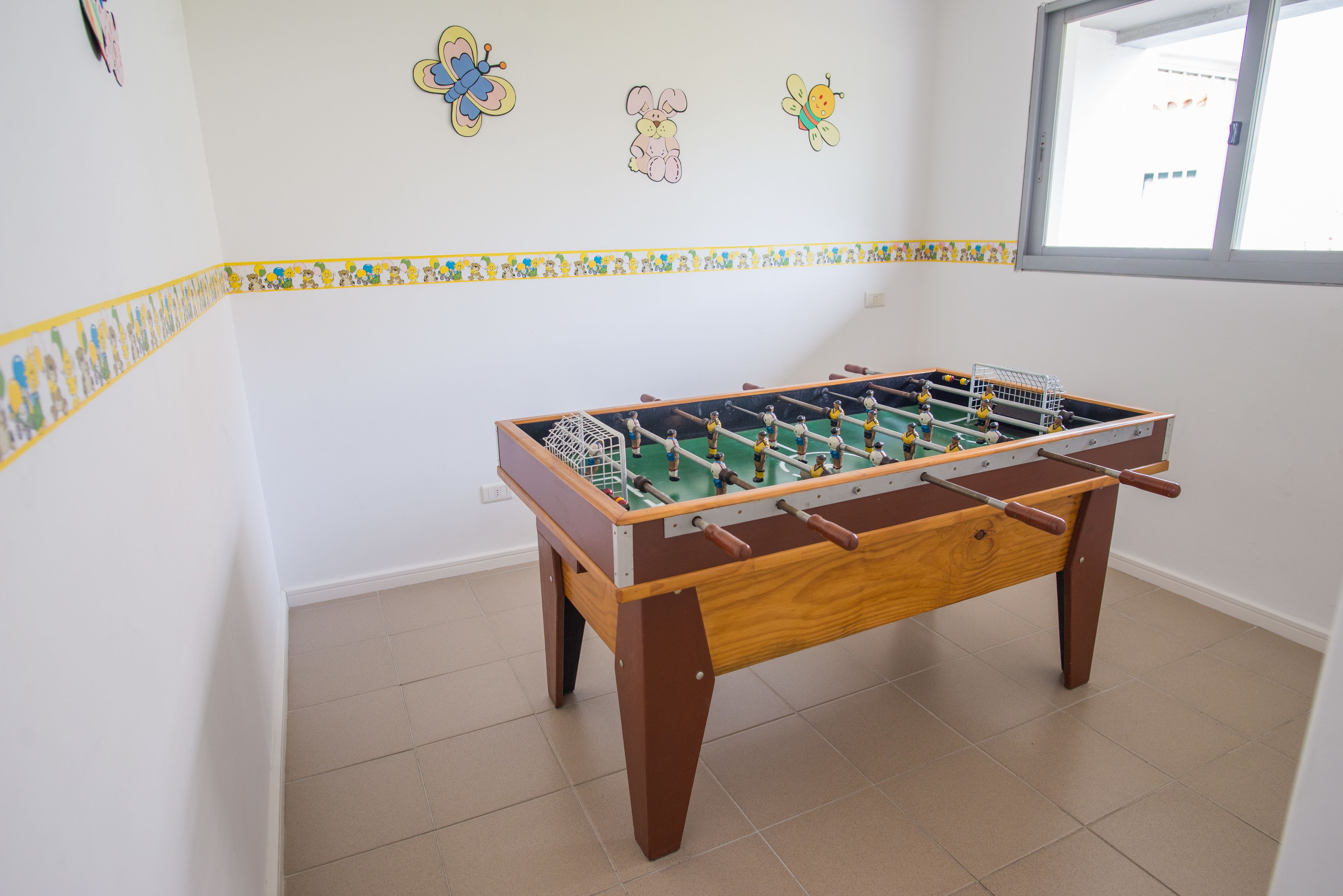 A foosball table in a room with tiled flooring and a window.