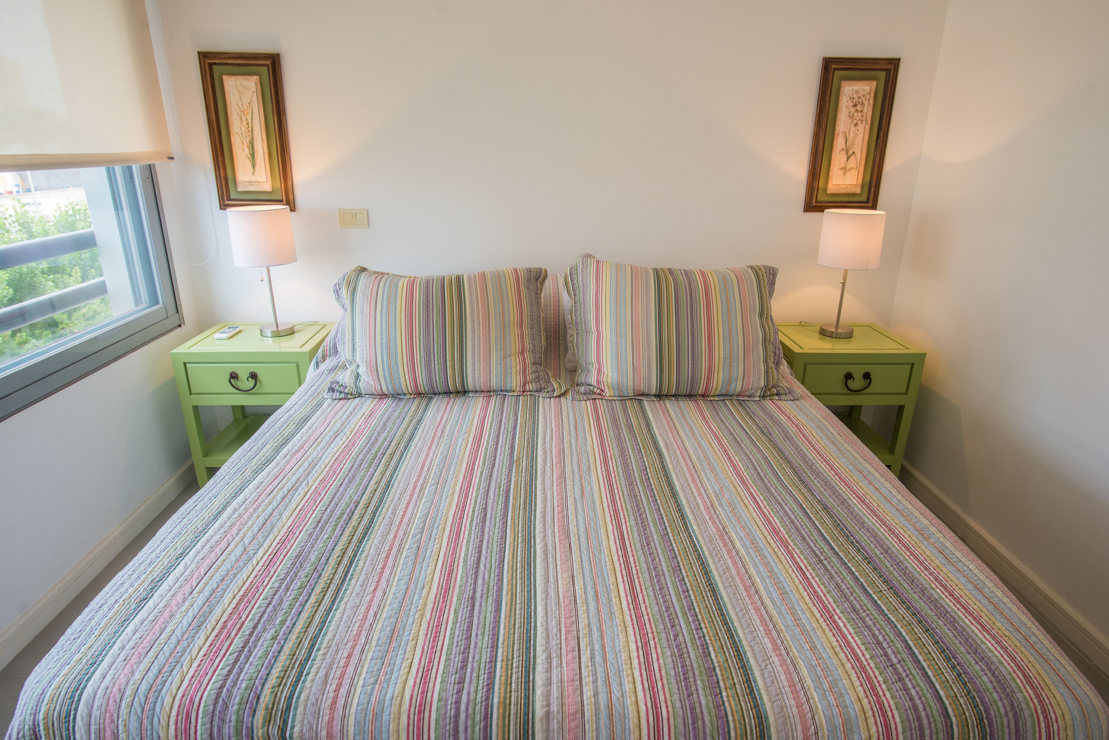Una cama con colcha a rayas, dos mesitas de noche con lámparas y cuadros en la pared.