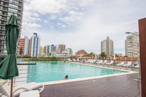 Piscina en la azotea con sillones de descanso y un paisaje urbano al fondo.