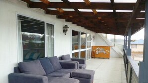 A covered outdoor seating area with a blue sectional sofa and a bench, a sign reading "Cheer Upstands", and a view of the street. - Mackenzie Lodge (Twizel)