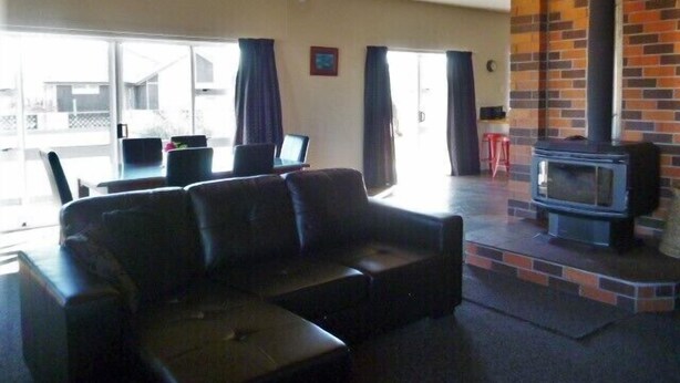 A living room with a black leather sofa, a dining table with chairs, a TV, and a fireplace. - Mackenzie Lodge (Twizel)