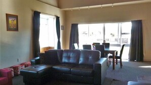 A living room with a sectional sofa, a dining table with chairs, and a large window with curtains. - Mackenzie Lodge (Twizel)