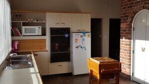 A compact kitchen with a microwave, oven, and refrigerator, wooden cabinets, a small wooden table, and a brick wall. - Mackenzie Lodge (Twizel)