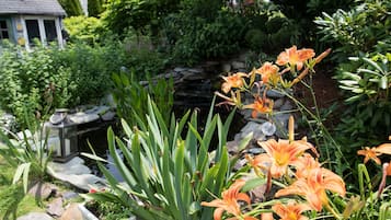 A garden with orange lilies, a stone pond, and a gazebo.