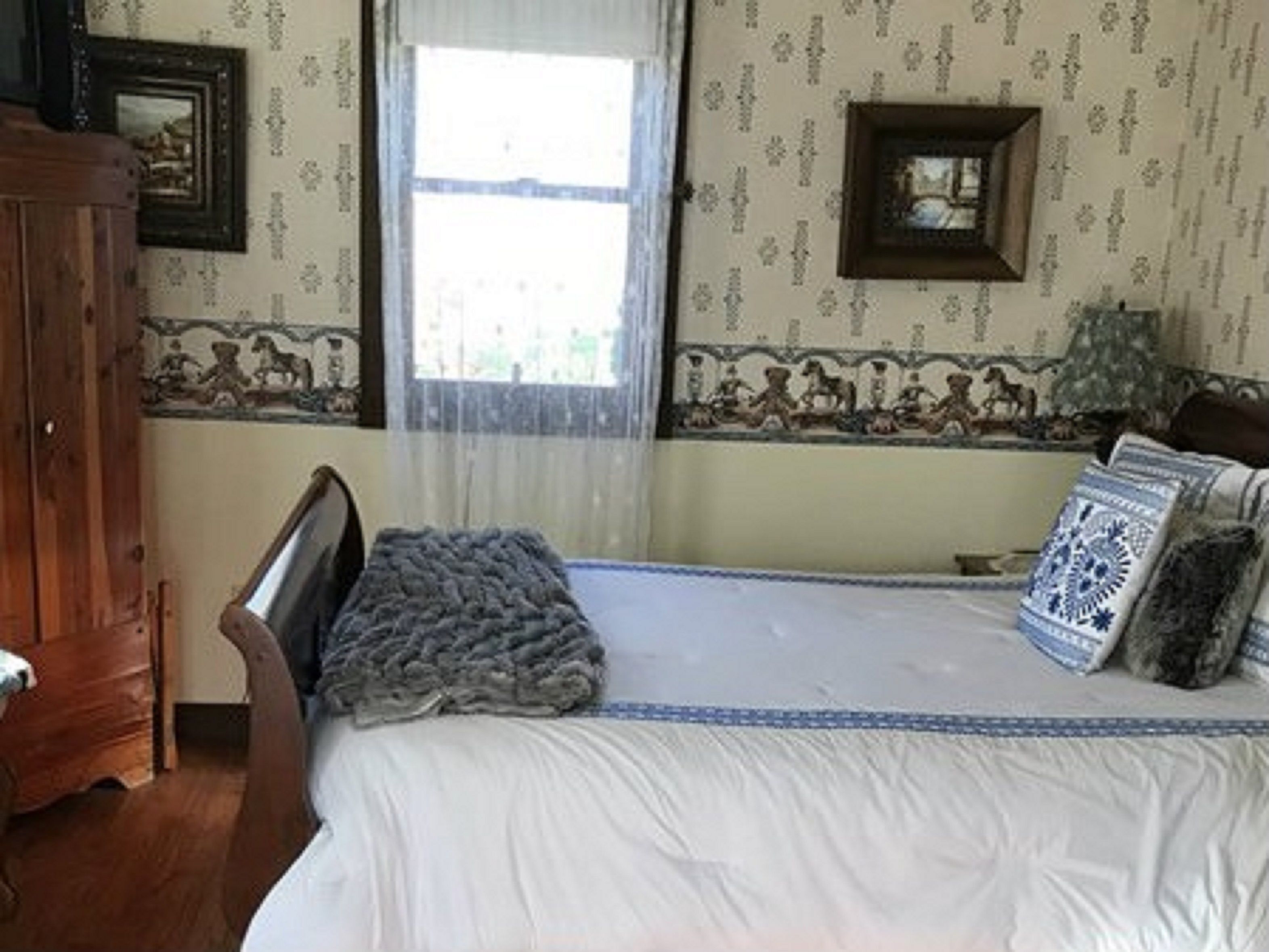 A bedroom with a wooden bed, a window with sheer curtains, and patterned wallpaper.