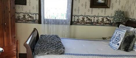 A bedroom with a wooden bed, a window with sheer curtains, and patterned wallpaper.