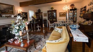 A cozy living room with a sofa, a dining table, and a fireplace. There are decorative items like candles and flowers on the table. - Gardenview Bed and Breakfast (Newport)