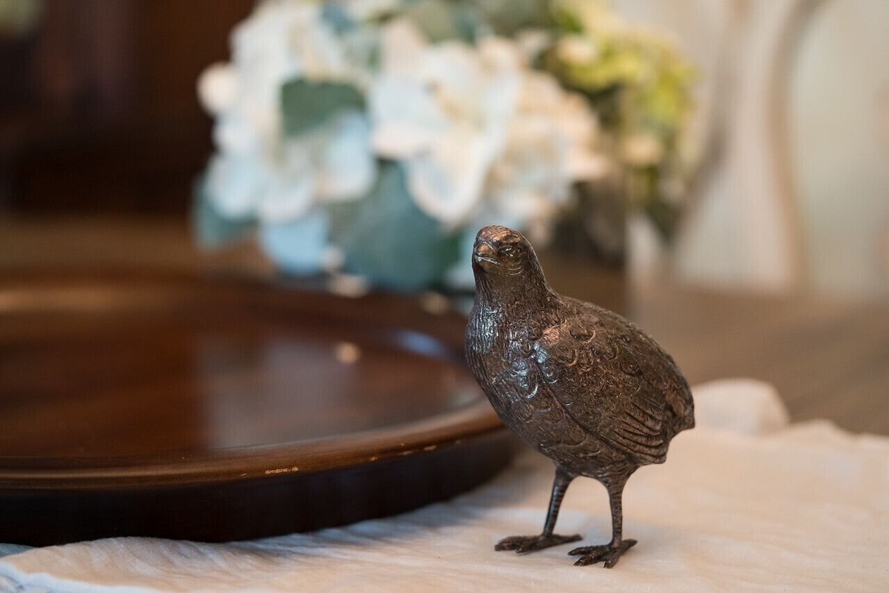A small bird figurine on a table with a blurred background of white flowers.