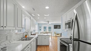 A modern kitchen with white cabinetry, stainless steel appliances, and a wooden floor. - Private pool and gorgeous beach house, steps from the ocean! (Surfside Beach)