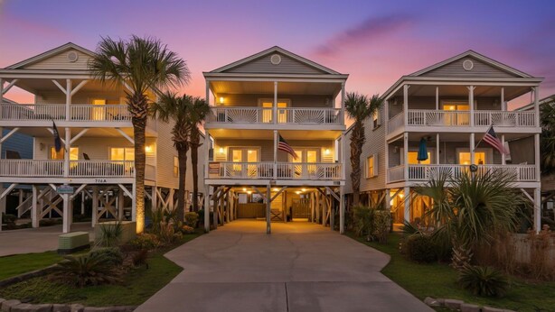 A beachfront hotel with multiple balconies, a covered walkway, and American flags. - Private pool and gorgeous beach house, steps from the ocean! (Surfside Beach)