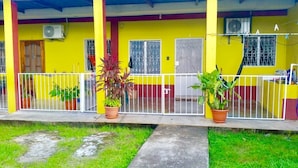 A yellow building with a covered porch, white railings, and potted plants.