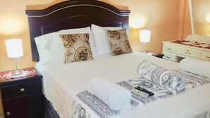 A neatly made bed with patterned pillows, a bedside table with a lamp, and a nightstand with a phone.