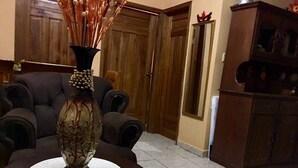 A room with a dark upholstered armchair, a decorative vase with dried reeds, and a wooden door in the background.