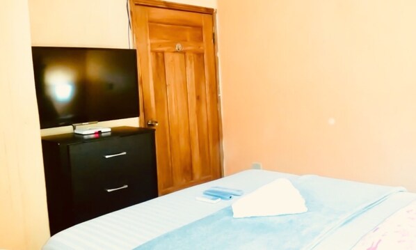 A bedroom with a bed, a TV on a dresser, and a wooden door. - TELA BEACH GETAWAY ☆ Apt #1 (Tela)