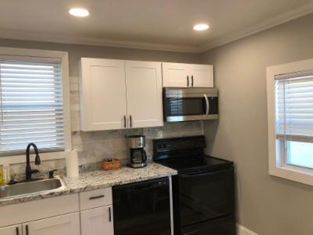 A compact kitchen with white cabinets, a black stove, a microwave, and a coffee maker.