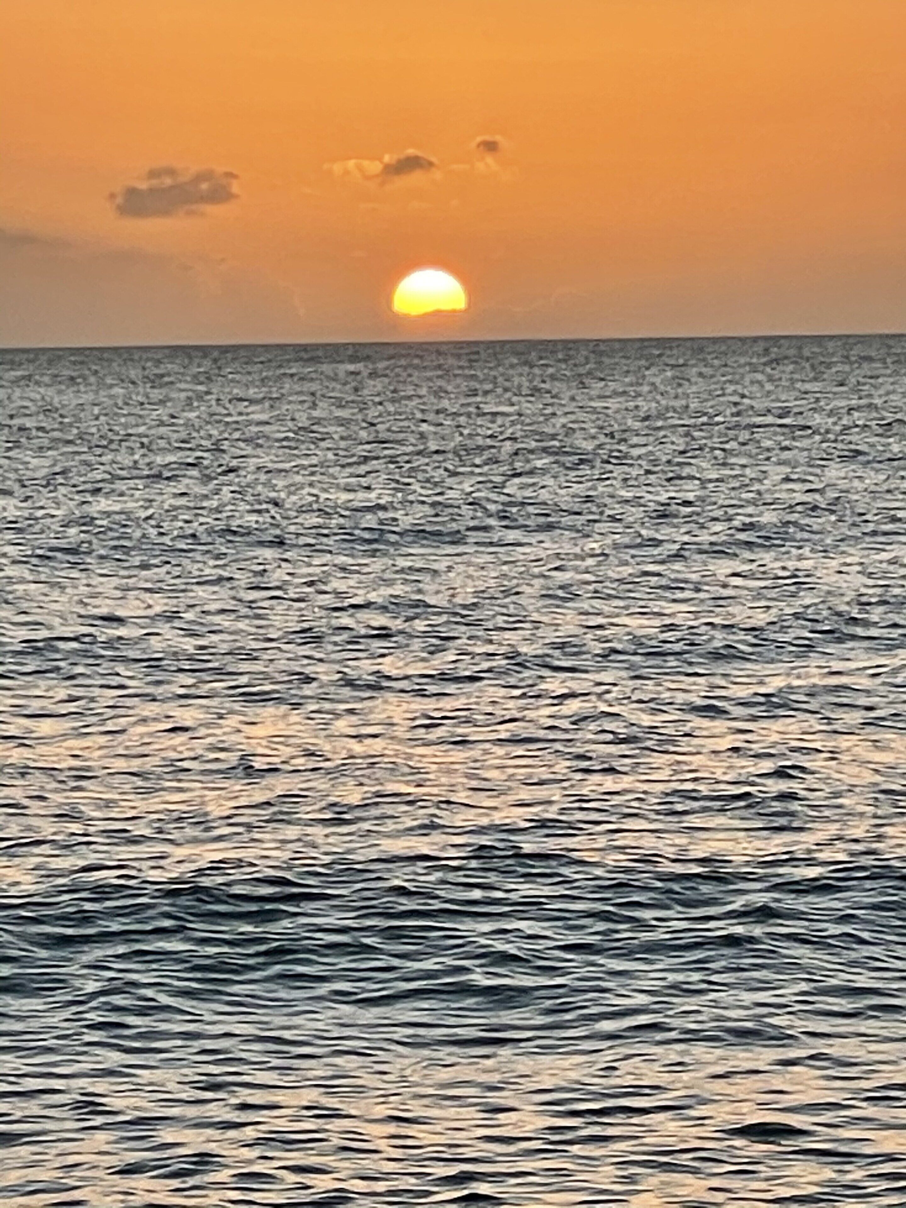 Een zonsondergang boven een kalme zee met een heldere horizon.