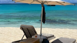 Ein Strand mit Liegestuhl und Sonnenschirm, einem Holztisch und einem Getränk.