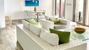 Ein modernes Wohnzimmer mit einem Ecksofa, einem Glastisch und einem Essbereich mit Tisch und Stühlen.