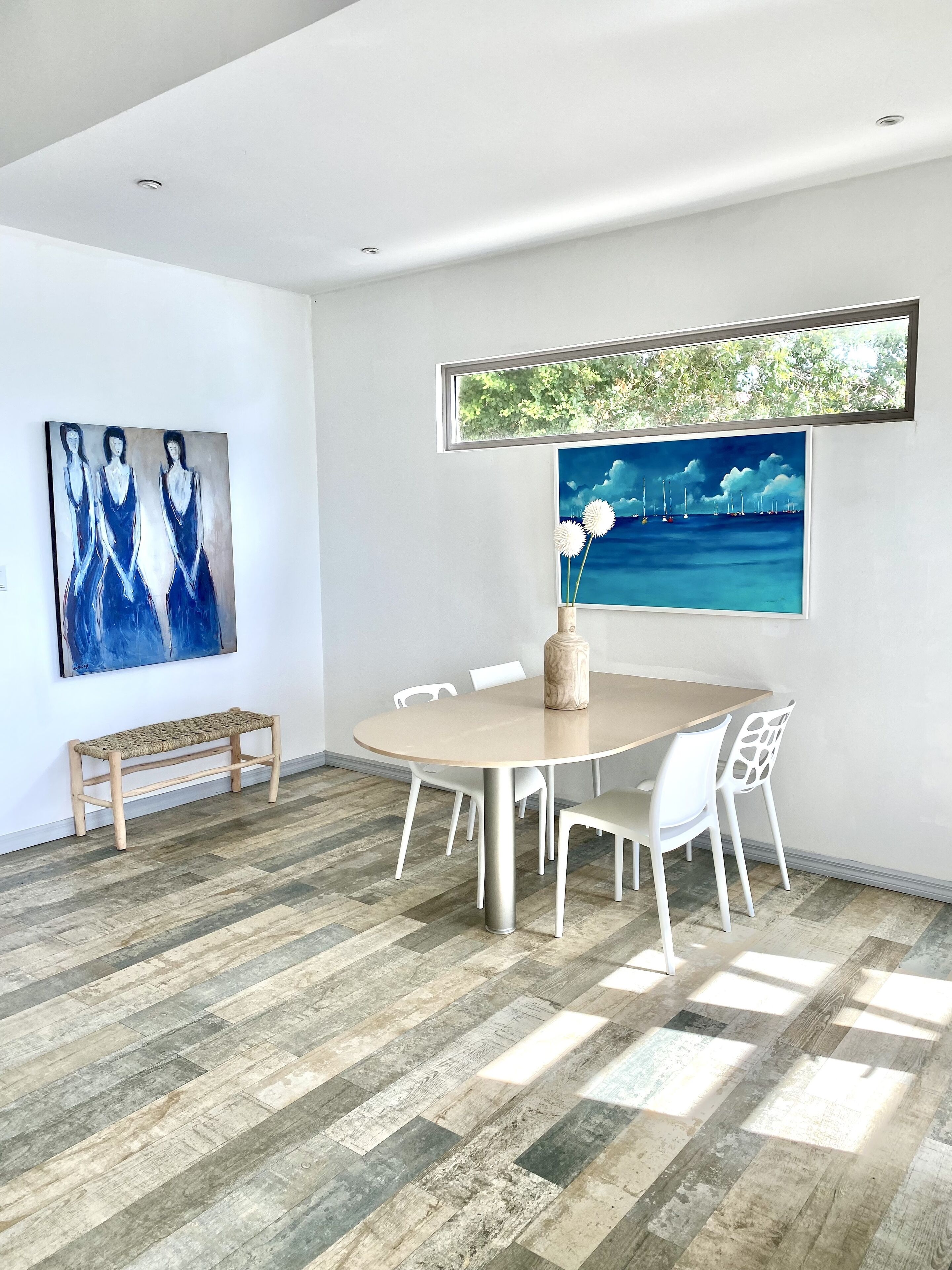 Un espace repas moderne avec une table ronde, des chaises blanches, un banc en bois et des œuvres d’art accrochées aux murs.