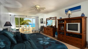 A hotel room with a large bed, a wooden dresser, a TV, and a balcony with a view of the ocean. - Restful Oceanfront 1BR, Northshore,  Low Density building with only 12 condos. (Cozumel)